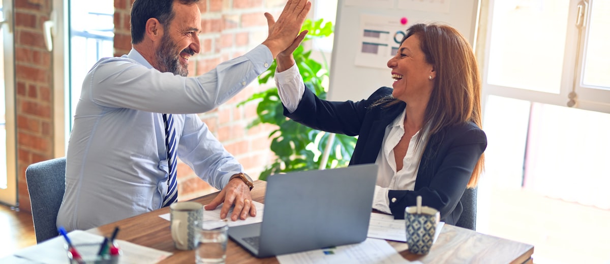 Two professionals shaking hands across a desk at the end of a meeting